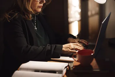 Business owner working on a laptop at a home office desk with a notebook and coffee cup